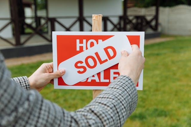 person placing sold sign over for sale sign